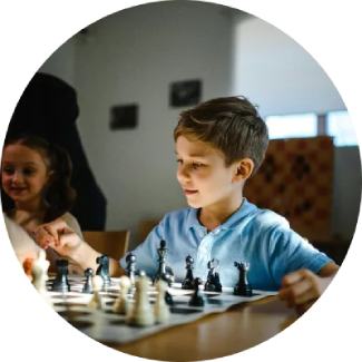 Niño con camisa azul jugando al ajedrez, centrado en el desarrollo de habilidades de pensamiento estratégico.