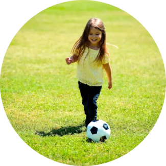 Niña con camiseta amarilla jugando al fútbol en un campo de hierba, disfrutando del juego activo.