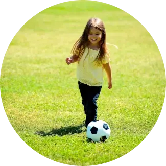 Girl in yellow top playing soccer on a grassy field, enjoying active play.