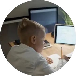 Child with blonde hair writing on paper at a desk.