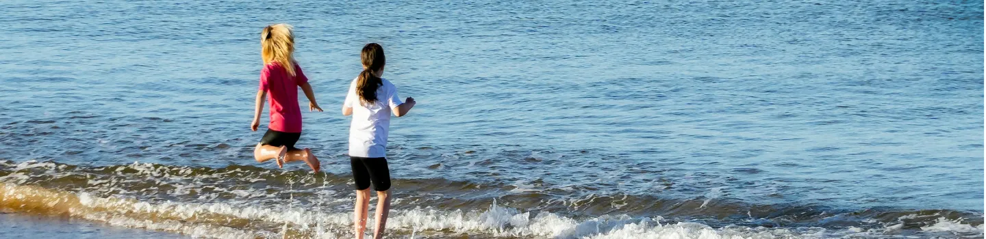 Two children playing by the seaside, splashing in gentle waves, showcasing ART Excel life skills.