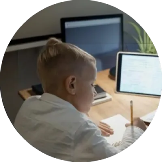 Child with blonde hair writing on paper at a desk.