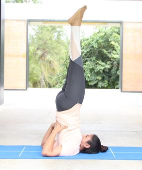 Yoga Sarvangasana - a girl lying on floor with her back stretched upwards