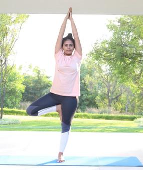 Yoga Vrikshasana - a girl standing with folded hands and one leg bent in tree pose