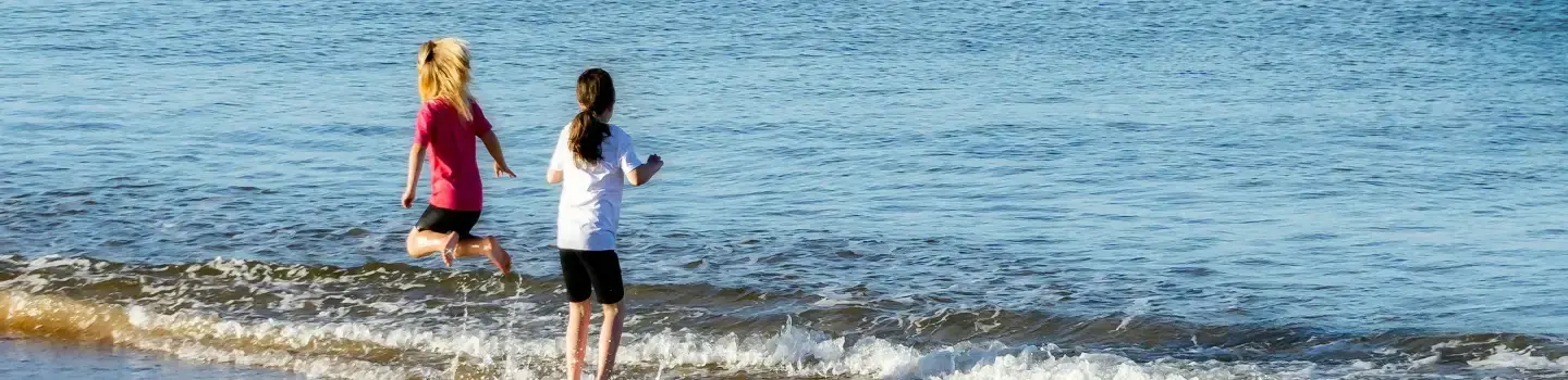 Deux enfants jouant au bord de la mer, s'éclaboussant dans de douces vagues, mettant en valeur les compétences de vie d'ART Excel.