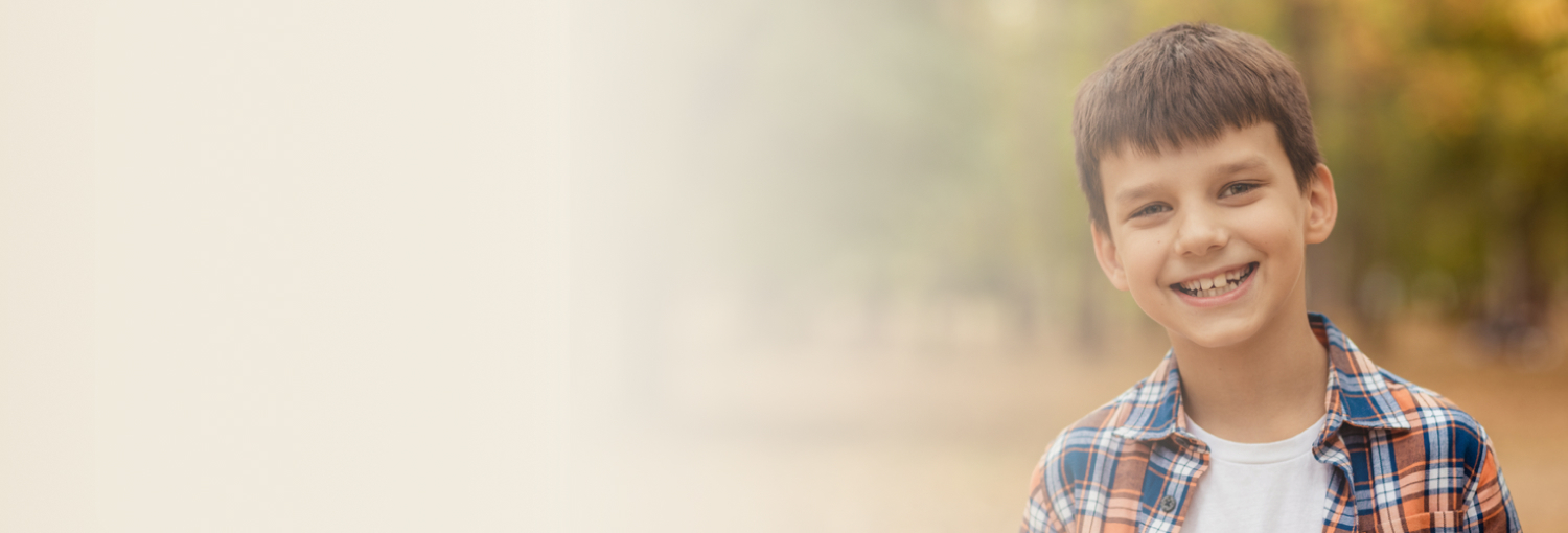 Young boy smiling gently, wearing a checkered shirt.