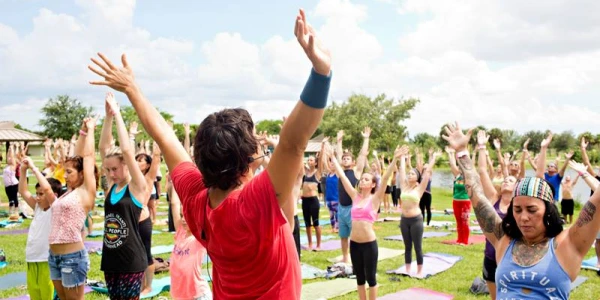 Grupo entusiástico de voluntários da Arte de Viver levantando as mãos em união durante um evento de serviço comunitário ao ar livre